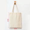 A beige canvas shopping tote bag hanging by its handle against a white background.