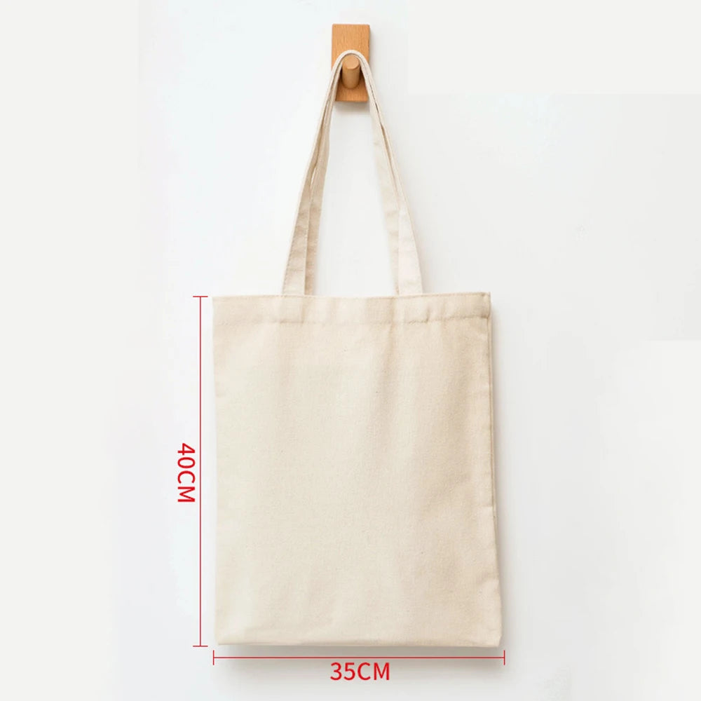 A beige canvas shopping tote bag hanging by its handle against a white background.
