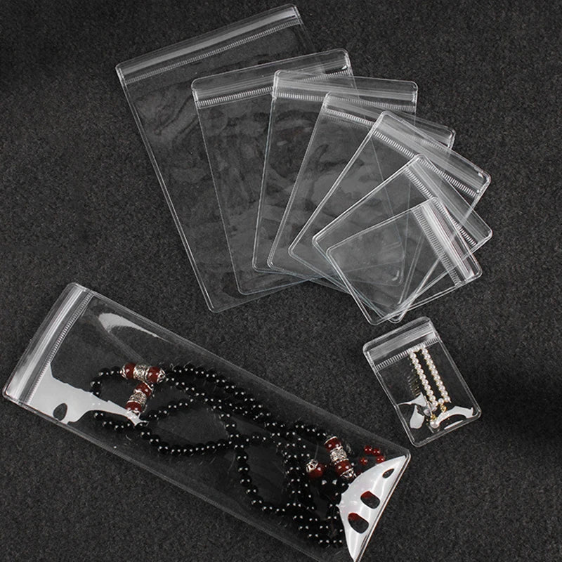 A transparent PVC jewelry pouch with a zip lock closure is shown alongside several stacked pouches and a beaded necklace.
