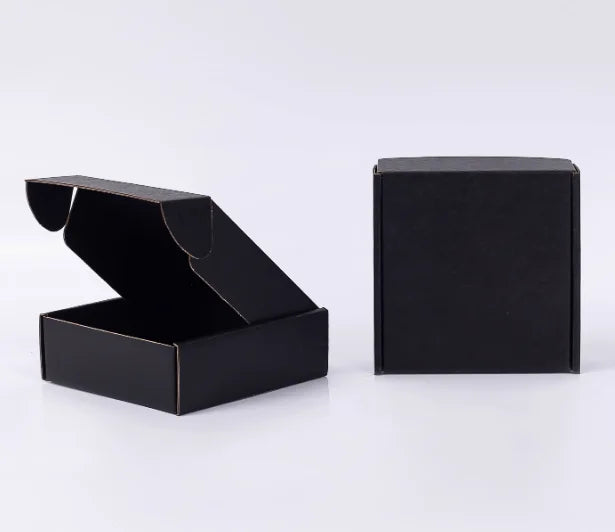 Eine schwarze Wellkartonschachtel, geöffnet und eine geschlossene Schachtel, auf einer weißen Oberfläche.