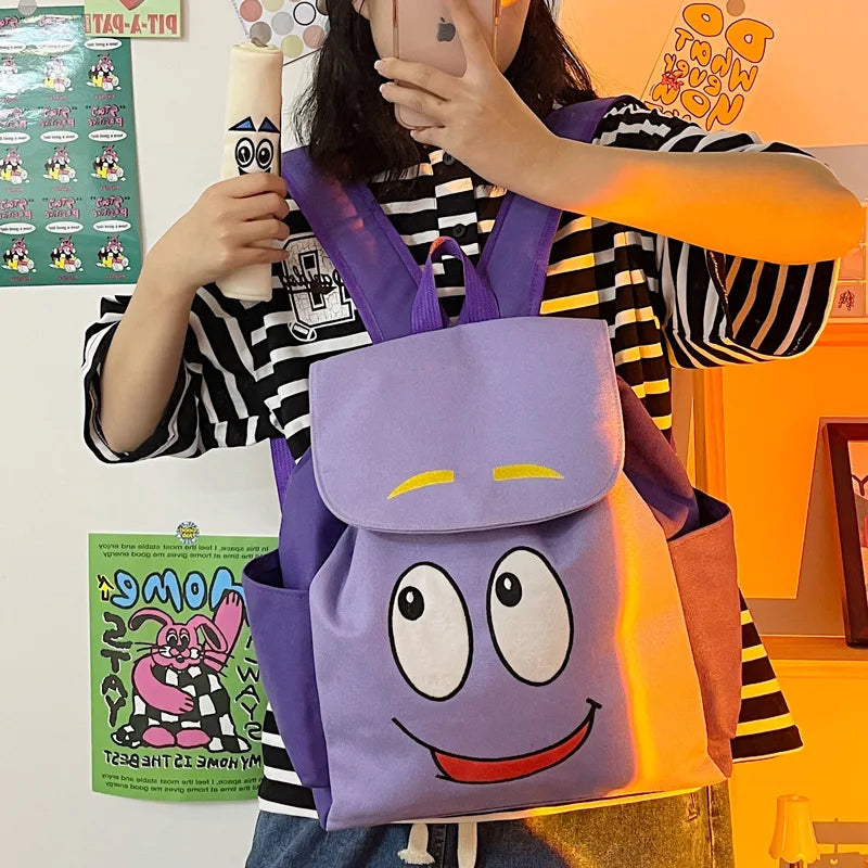 Eine Person hält einen lila und orange Dora The Explorer Flanell-Rucksack vor einem orangen Hintergrund.