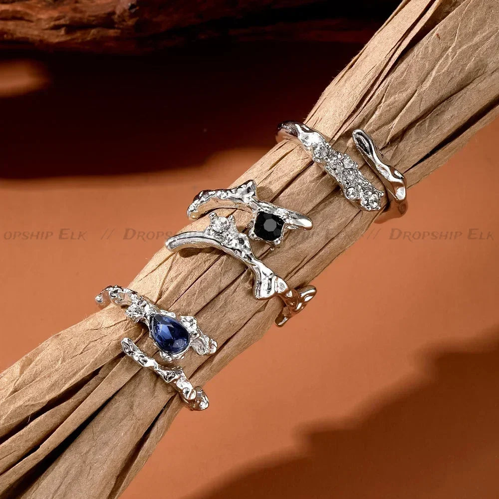 A close-up of silver irregular heart-shaped rings displayed on a natural wood branch.