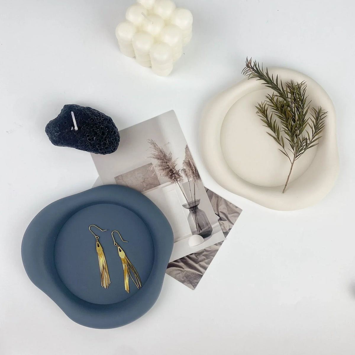 A set of light blue silicone coasters with gold-toned jewelry and a sprig of greenery on a white background.
