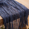 A dark blue crinkle gauze cheesecloth table runner draped on a wooden table.