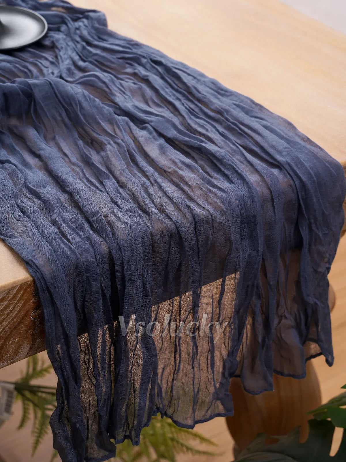 A dark blue crinkle gauze cheesecloth table runner draped on a wooden table.