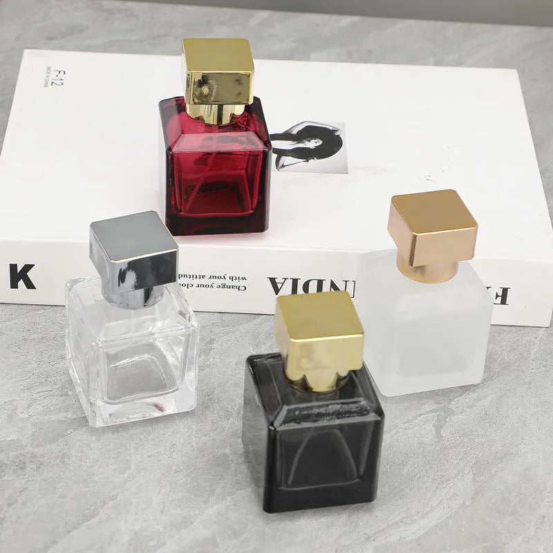 A collection of glass perfume bottles in various colors and shapes with gold sprayers displayed on a white box.