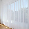 Durchsichtige weiße Tüllvorhänge mit vertikalen Falten, die ein Fenster mit natürlichem Licht bedecken.