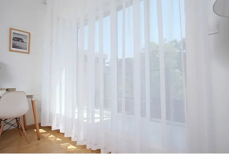 Durchsichtige weiße Tüllvorhänge mit vertikalen Falten, die ein Fenster mit natürlichem Licht bedecken.