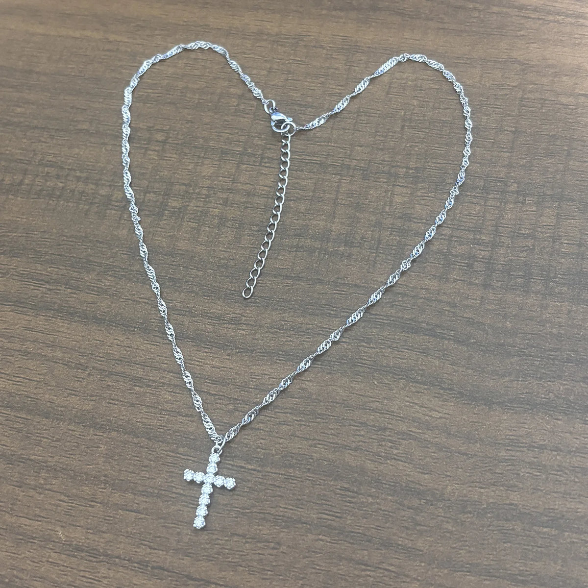 Un collier croix argenté avec une chaîne suspendu sur un fond en bois.