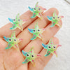 Several small, starfish-shaped resin charms in shades of green and pink are held in a person's hand.
