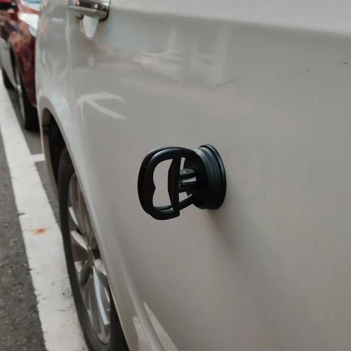 Close-up of a black car dent puller kit handle mounted on the side of a white car.