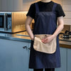 A person wearing a dark blue striped kitchen apron with a removable beige towel in a modern kitchen setting.
