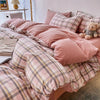 Pink and gray plaid bedding set featuring a duvet cover, flat sheet, and pillows on a bed.