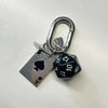 Silver keychain charm featuring a heart design and a D-shaped buckle, attached to a silver tag and a black dice.