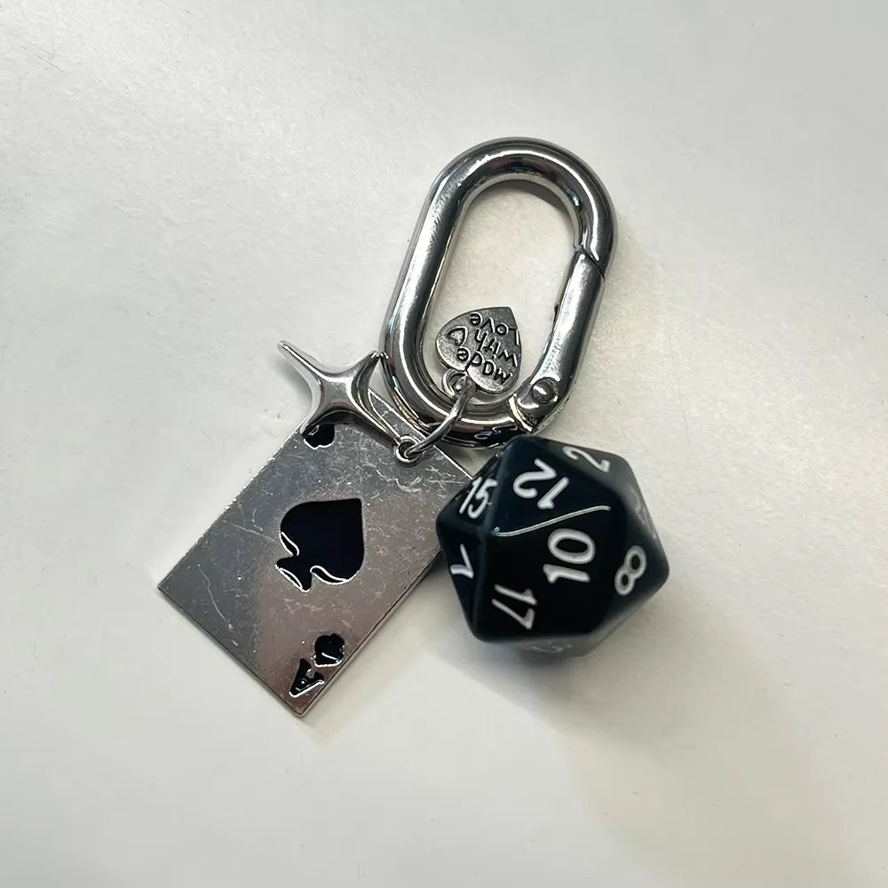 Silver keychain charm featuring a heart design and a D-shaped buckle, attached to a silver tag and a black dice.