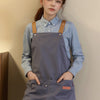 A young woman wearing a gray adjustable polyester kitchen apron over a light blue shirt.