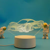 A wireframe 3D illusion light sculpture of a car floats above a white base with two small astronaut figures.