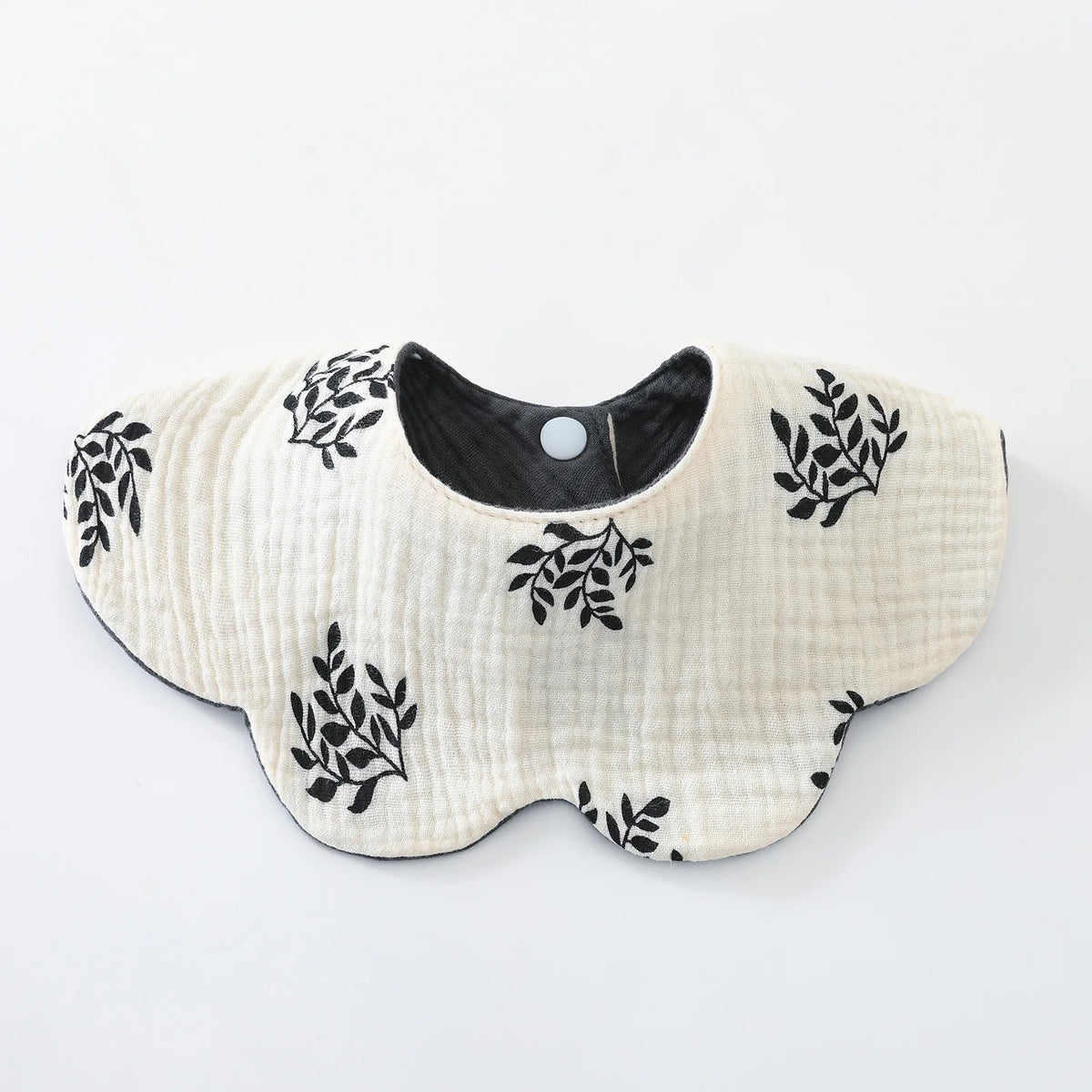 A light beige cotton baby feeding bib with black leafy embroidery and a dark center