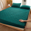 A teal quilted mattress protector with extra padding is shown on a wooden bed frame.