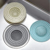 A set of three silicone sink drain filters or strainers in various shades of light green and gray resting on a metal tray.