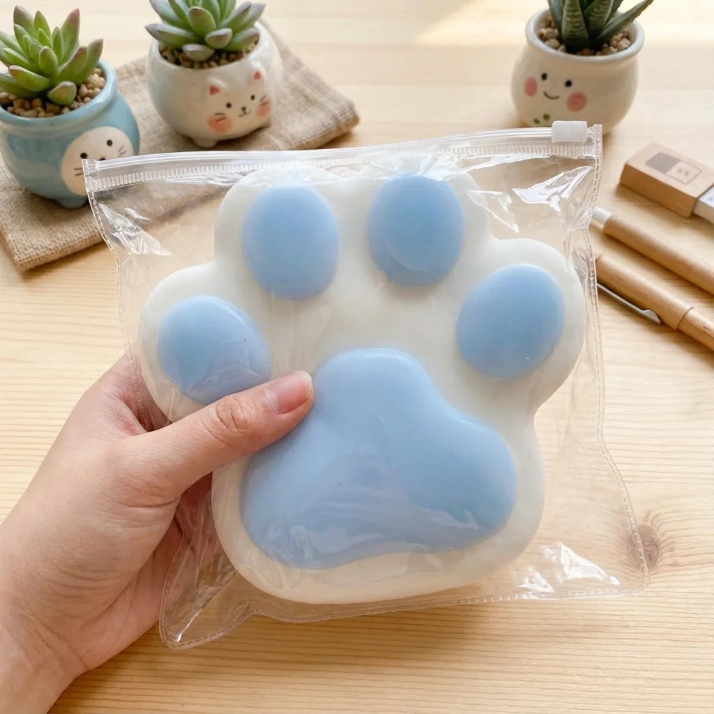 A hand holds a soft, light blue silicone cat paw squeeze toy for stress relief.