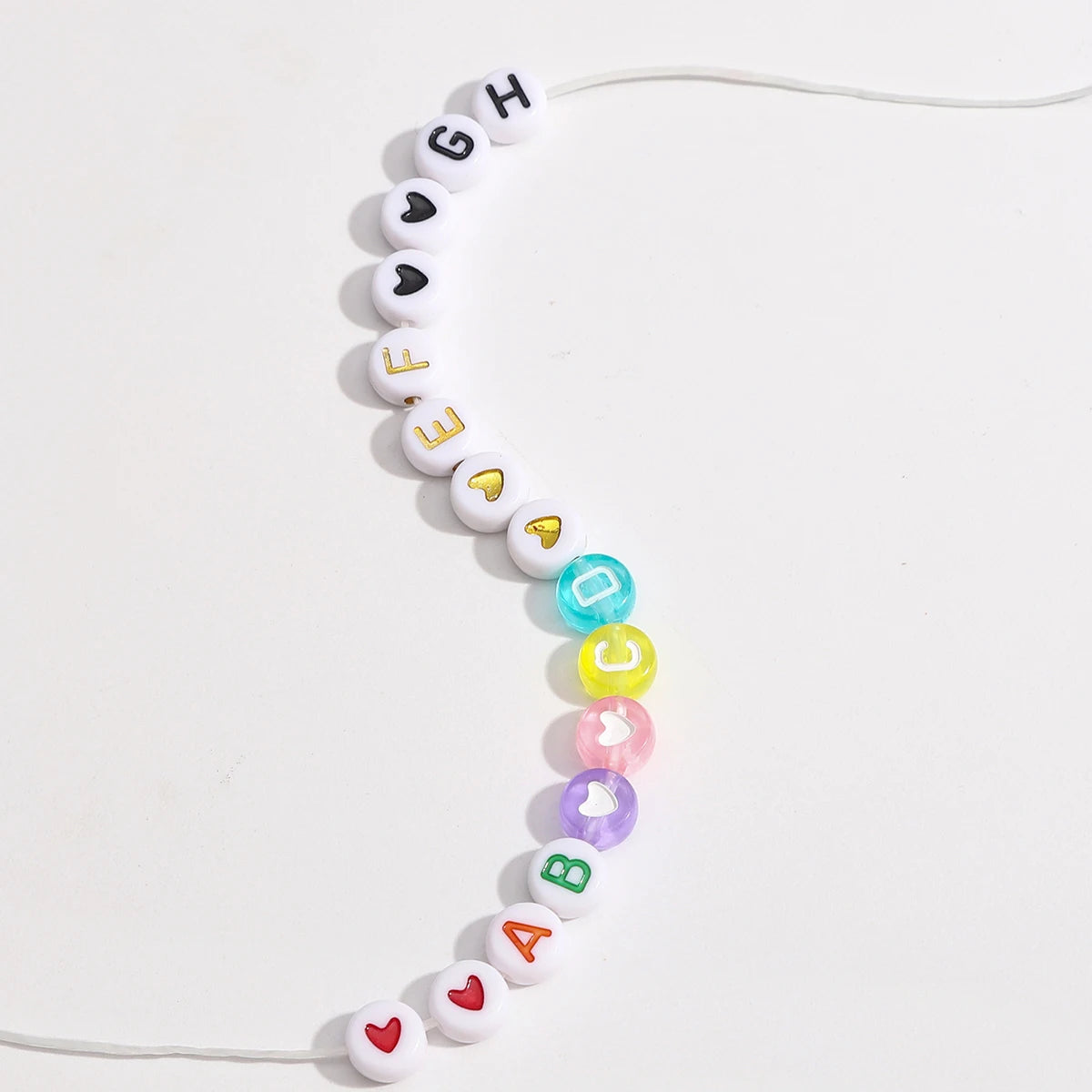 A string of acrylic letter beads spelling out 'G H E F E D C' arranged in a curved line against a white background.