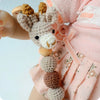 A wooden pacifier clip featuring a crochet bead chain in beige and brown colors attached to a pink baby outfit.