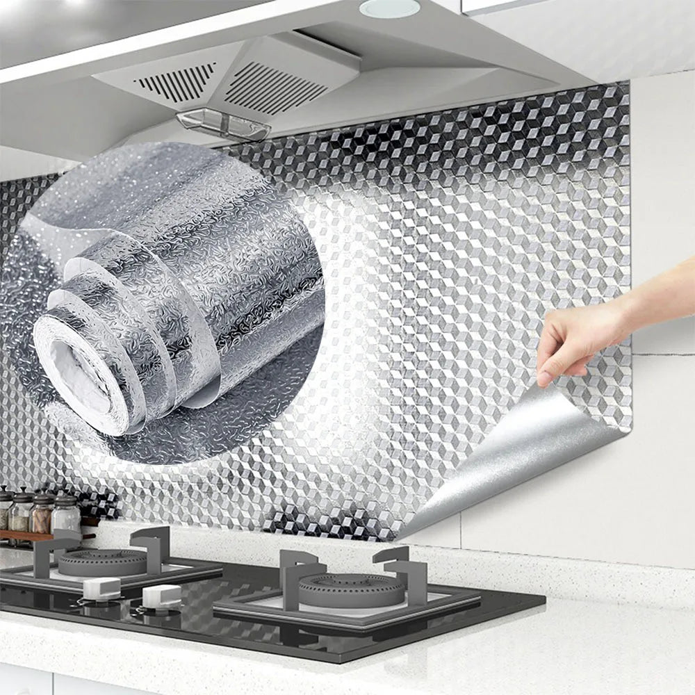 A hand is applying self-adhesive aluminum foil to a kitchen backsplash surface.