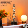 A black, wavy seaweed-shaped desk lamp with a soft white glow illuminates a wooden surface.