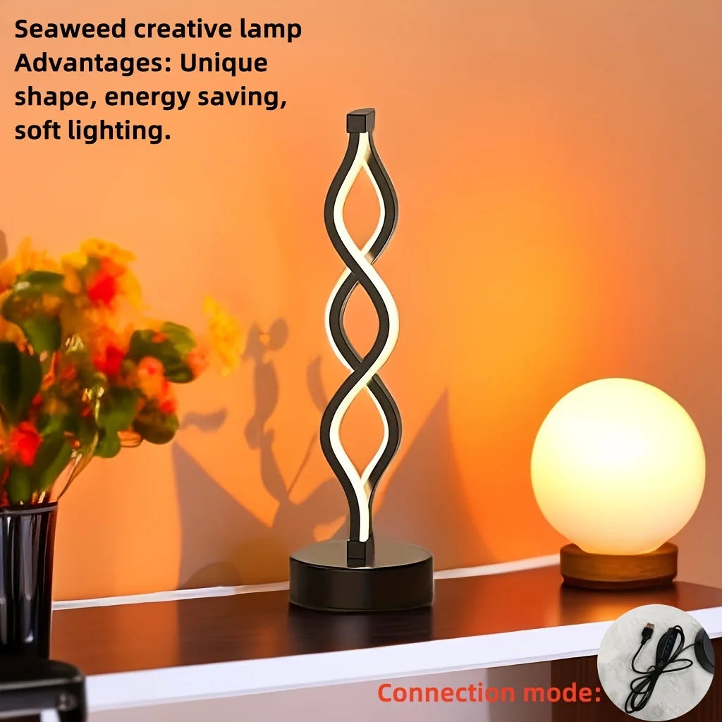 A black, wavy seaweed-shaped desk lamp with a soft white glow illuminates a wooden surface.