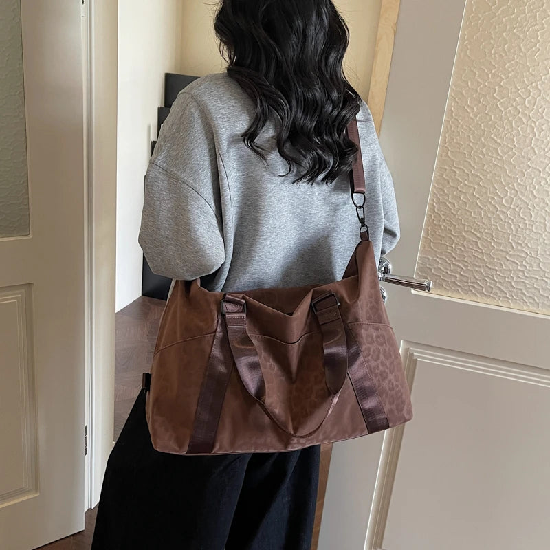 A woman is holding a brown leopard print duffle bag with an adjustable strap in a light-colored room.
