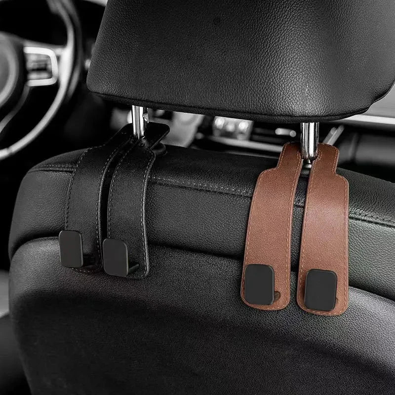 Car headrest hooks in brown leather attach to a black car seat for bags and organizers