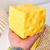 A hand holds a bright yellow, squishy, cheese-themed stress relief toy against a woven background.