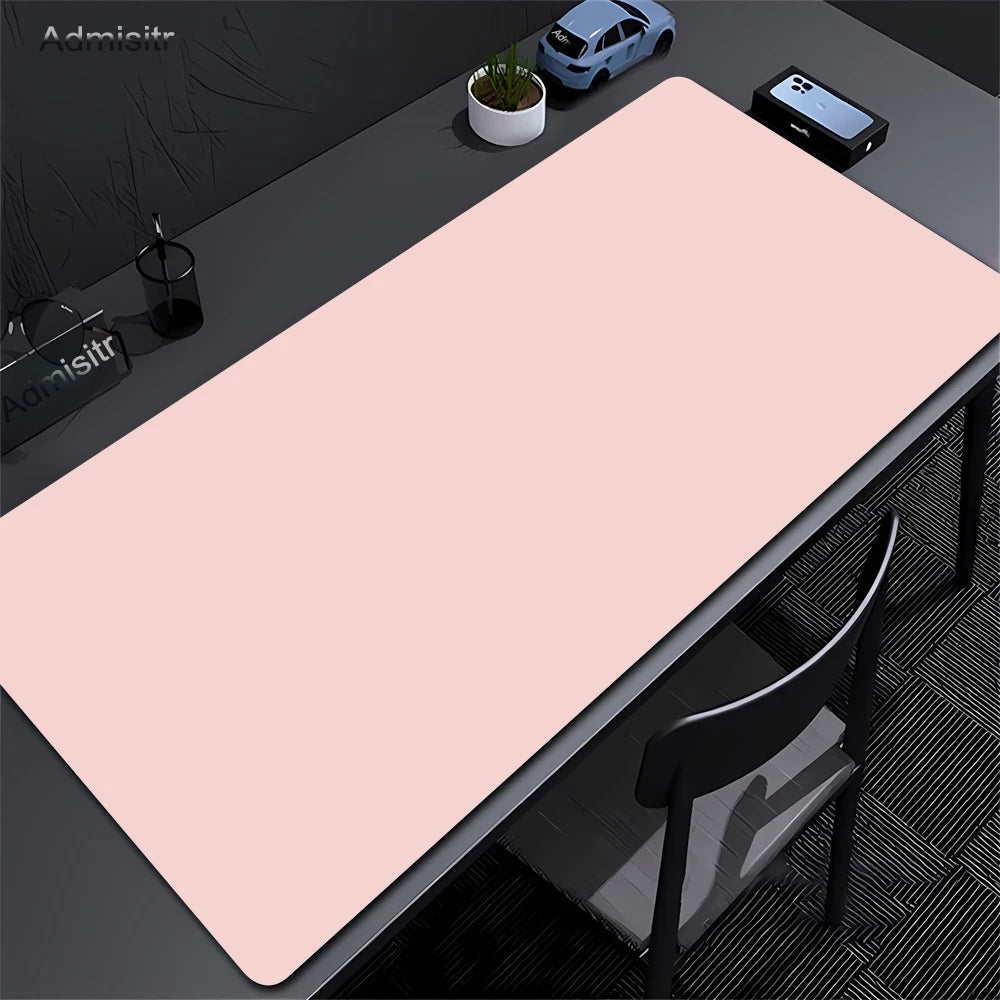 A large pink non-slip desk mat is shown on a dark desk with a chair and a small potted plant.