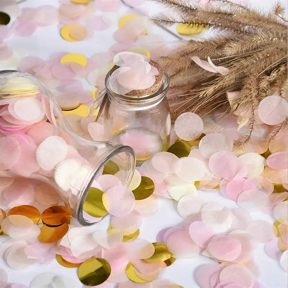 Rosa und goldener Papierschnipsel-Confetti auf weißer Fläche neben einem Glasgefäß