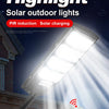 A spotlight solar outdoor light is mounted on a wall, with a hand holding a remote control nearby.