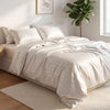 A white satin striped jacquard duvet cover set displayed on a bed with natural light and a potted plant in the background.