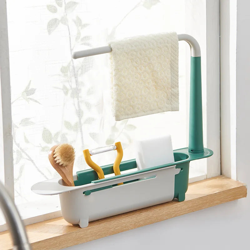 A teal and white adjustable sink sponge holder with a hanging towel rack and drainer basket on a wooden shelf.