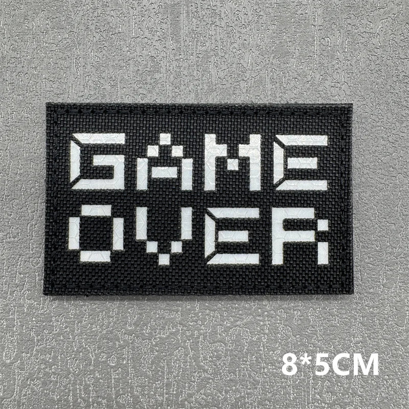 Black embroidered patch with white text GAME OVER on a gray background