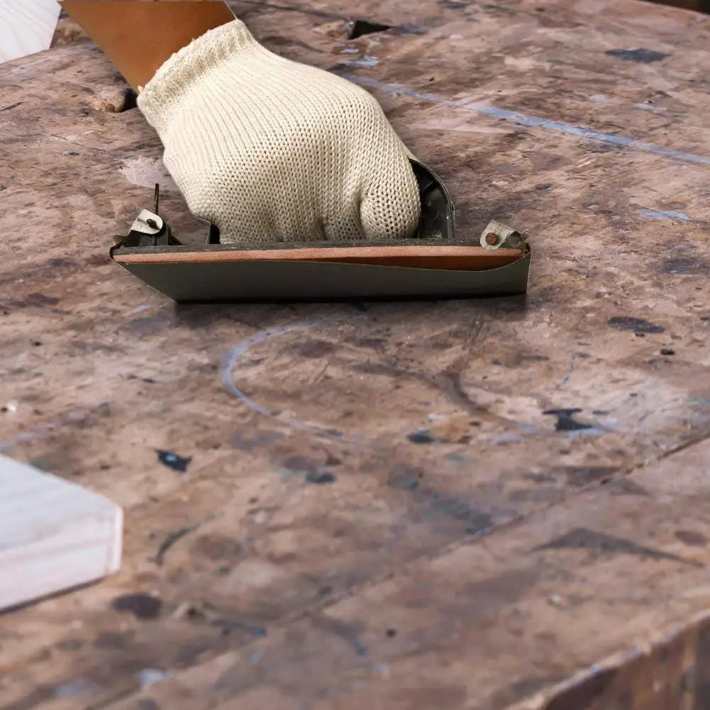 A beige knitted glove is resting on a piece of sandpaper within its holder on a wooden surface.