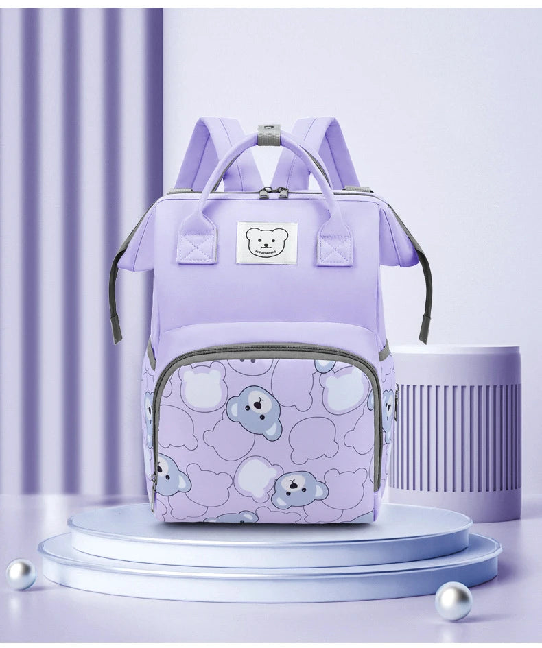 A purple waterproof diaper backpack with a bear print design is displayed on a light blue pedestal.