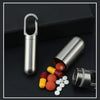 Stainless steel pill capsule with keychain and loose pills on a dark surface