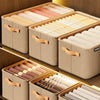 A set of beige fabric storage boxes with wooden handles and folded fabric items displayed on a wooden shelf.