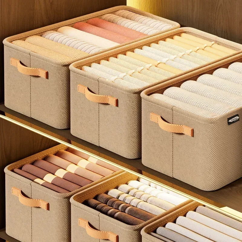 A set of beige fabric storage boxes with wooden handles and folded fabric items displayed on a wooden shelf.