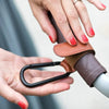 A hand is holding a brown and gray stroller hook with a PU leather baby bag organizer.