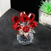 A sculpture of red crystal roses with a silver base and green foliage displayed on a dark surface.