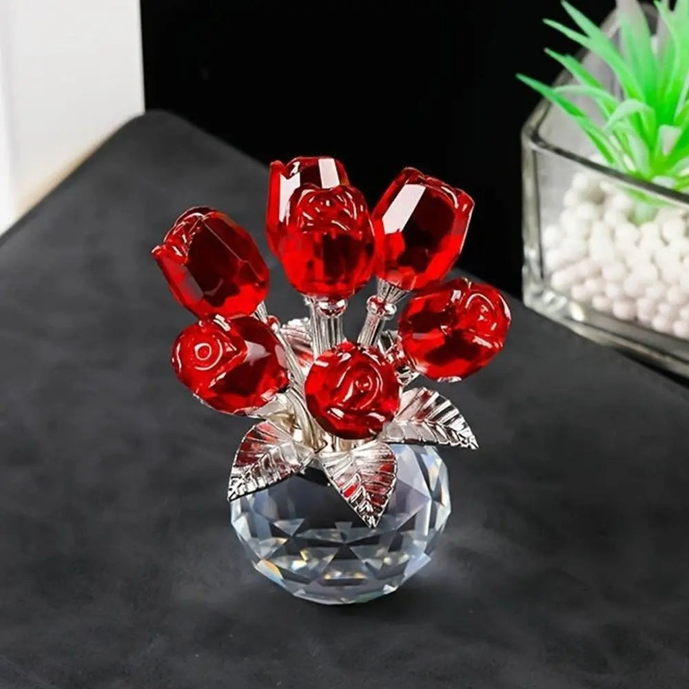 A sculpture of red crystal roses with a silver base and green foliage displayed on a dark surface.