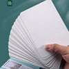 A stack of white thickened paper sheets is shown next to a tin box containing watercolor paper.