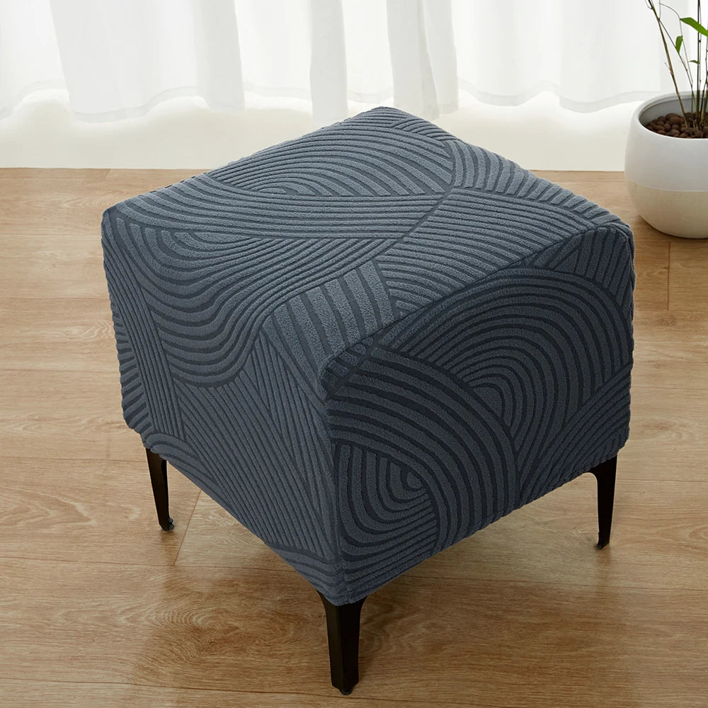 A dark blue geometric jacquard stretch ottoman cover placed on a wooden floor.