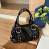 A black soft PU leather shoulder bag with silver rivet accents resting on a wooden surface.